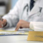 A physician works on papers. Focus is on a plaque in the foreground with Urologist written on it.